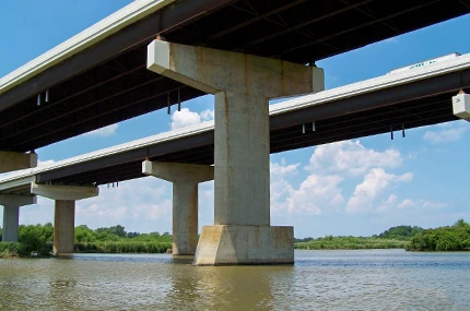 Two parallel concrete highway bridges span across a river, supported by large pillars, with trees and sky visible in the background.