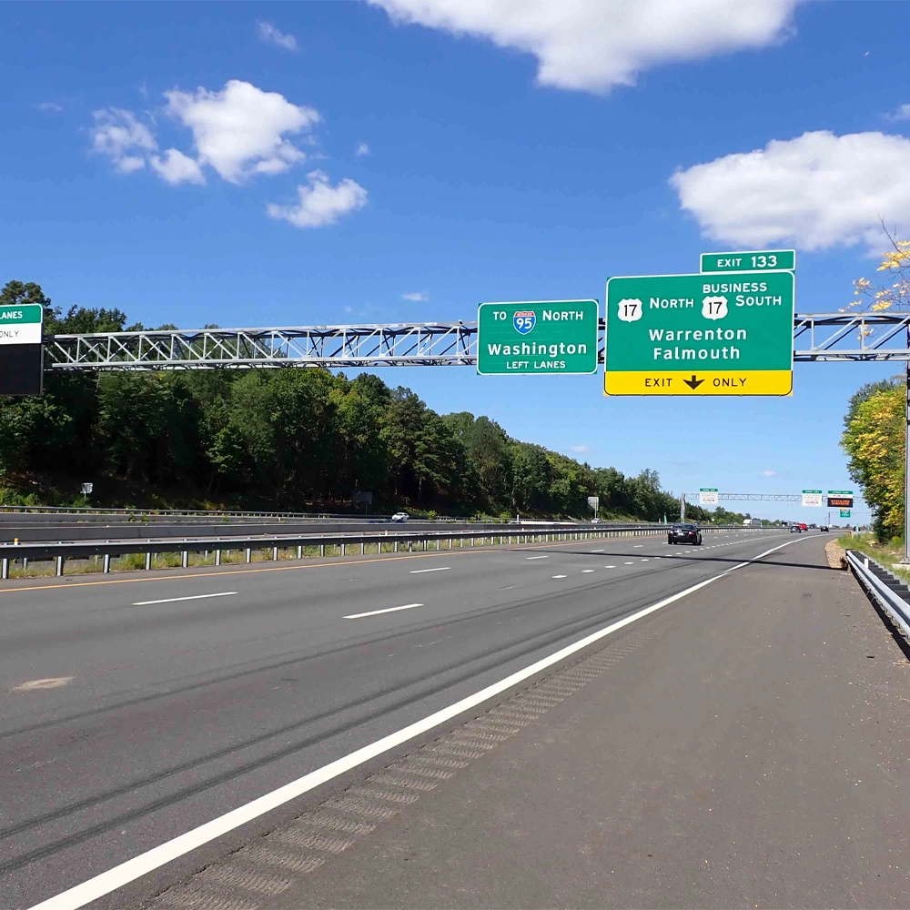 An empty multi-lane highway with green exit signs overhead for Interstate 95 North and Business Route 17 toward Warrenton and Falmouth under a blue sky with some clouds.